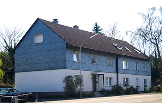 Zweistöckiges Wohnhaus mit grauer Schieferfassade im oberen Bereich und weißem Putz im unteren Bereich an einer Straße mit parkenden Autos