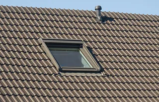Dachflächenfenster in einem mit braunen Dachziegeln gedeckten Dach neben einem Lüftungsrohr