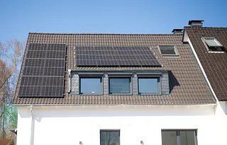 Hausdach mit mehreren Solarpanelen und drei Dachfenstern